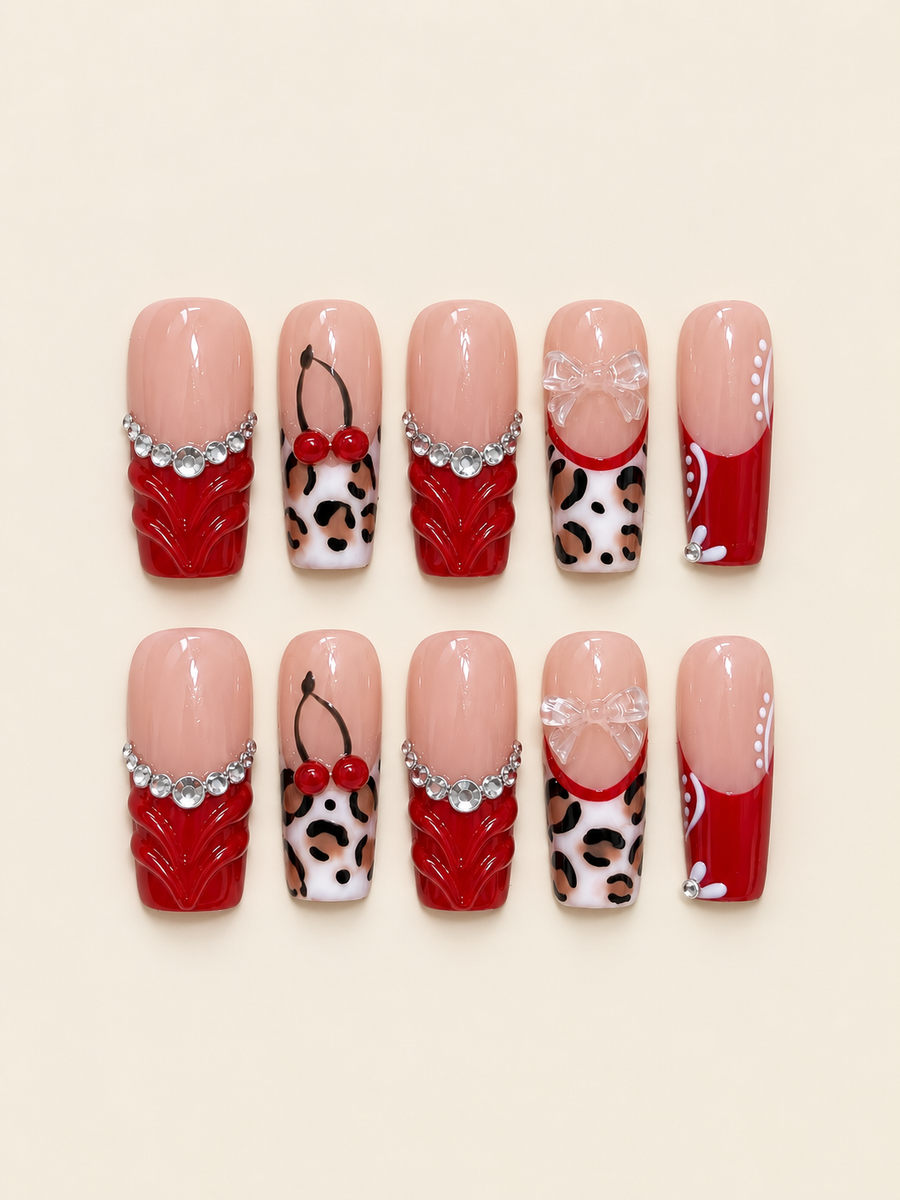 Ten glossy square press-on nails in red and nude with sculpted red accents, raised cherries, clear bows, leopard spots, and rhinestones