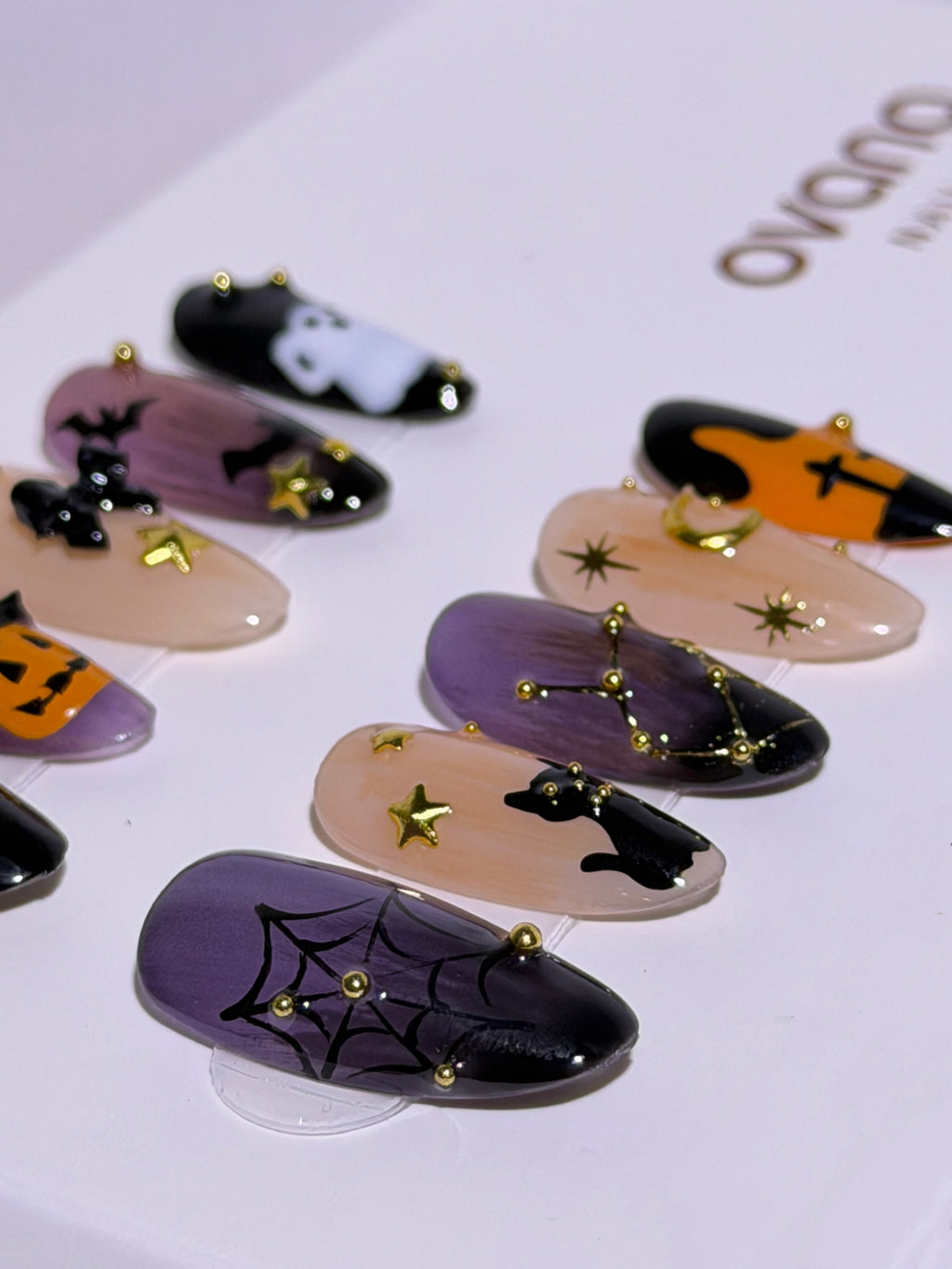 Ten Halloween almond press-on nails in purple, peach, orange, and black with a pumpkin, ghost, black cat, bats, spiderweb, and gold accents