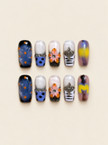 Ten glossy square press-on nails with raised peach-and-orange flowers, blue nails with orange dots, jeweled crosses, and violet-yellow swirls